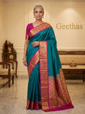 Model wearing a teal blue semi silk saree with magenta zari border and ornate pallu