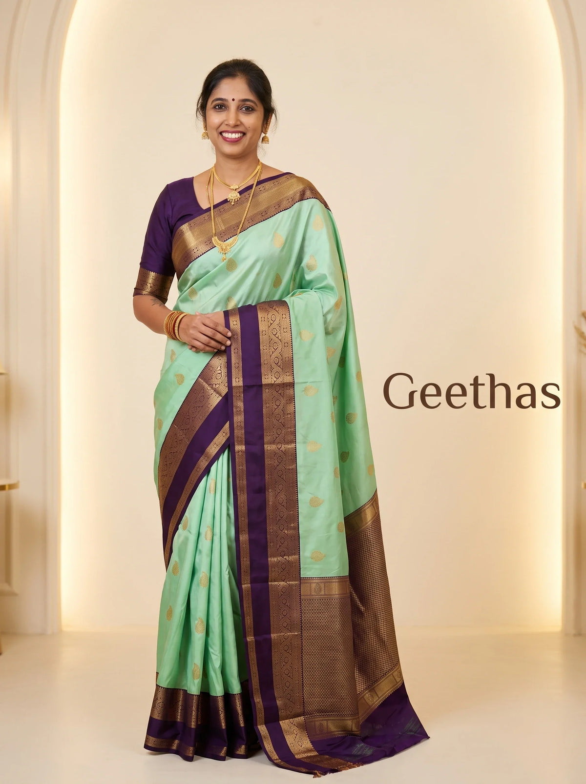 Model wearing a mint green soft silk saree with gold-toned woven motifs and a deep purple decorative border.