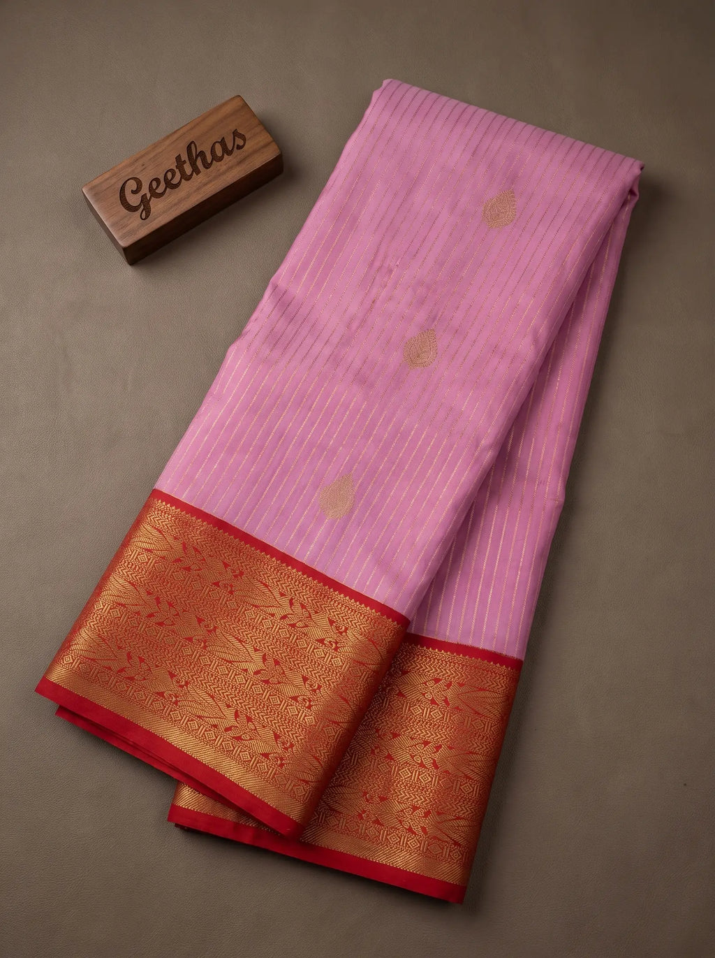 Lilac pink soft silk saree displayed with fine gold-toned stripes, woven motifs and a rich reddish zari border