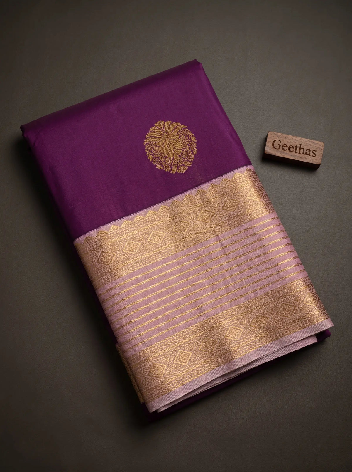 Folded deep purple soft silk saree with gold-toned floral motif and lilac zari-woven border