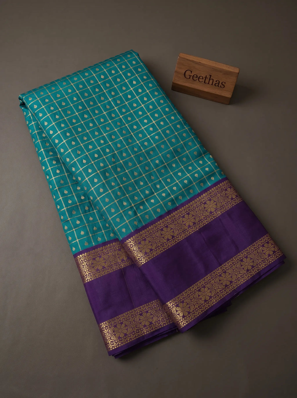 Teal blue soft silk saree with gold-toned geometric motifs and deep purple woven border