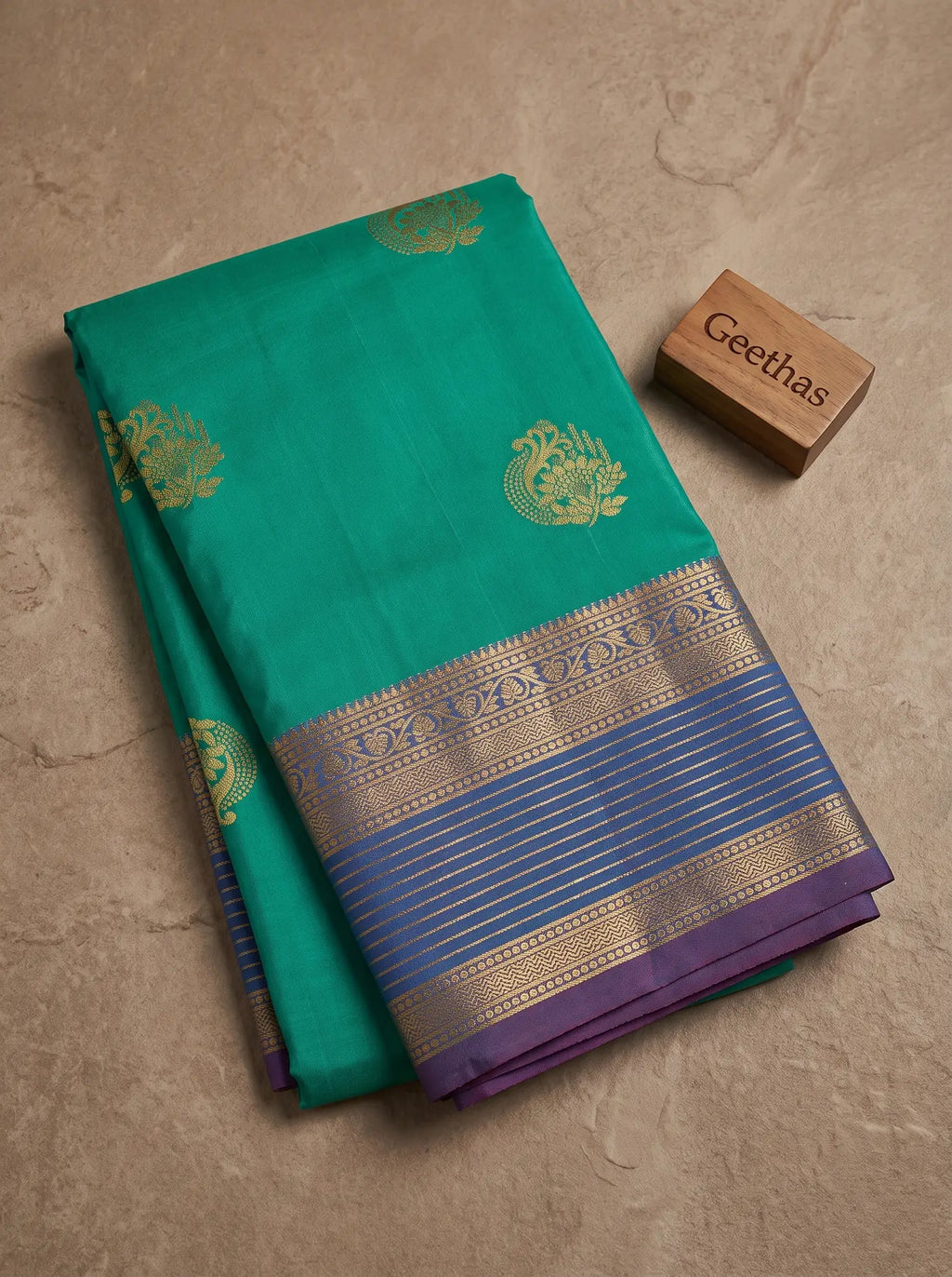 Folded sea green soft silk saree showing gold-toned woven motifs and a purple border with intricate detailing.