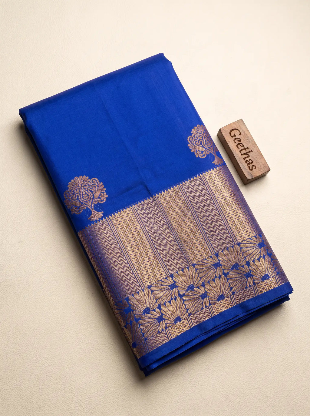Folded royal blue soft silk saree showing gold-toned floral motifs and an intricate woven border