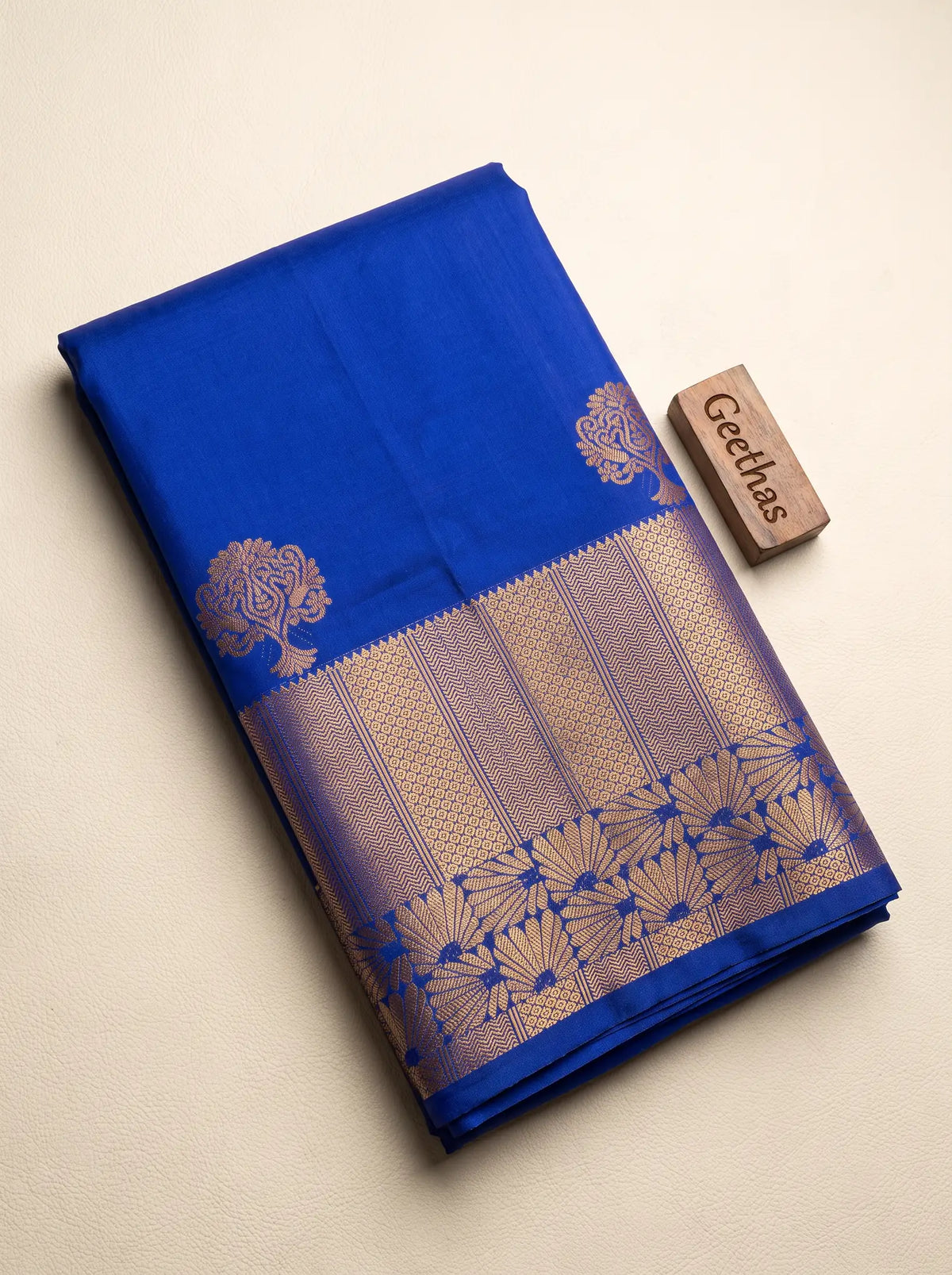 Folded royal blue soft silk saree showing gold-toned floral motifs and an intricate woven border